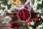 Bildet viser bringebær, epler, kjeks, en melkemugge og blomster på et bord