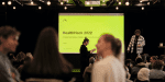 Yellow screen with the text HealthHACK 2022, and people infront of the screen mingeling.