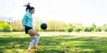 Mørkhåret jente med turkis overdel trikser med fotball på gresslette