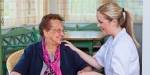 En sykepleier holder en eldre dame i hånda.