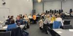 Mange menneske sit i grupper på ein workshop