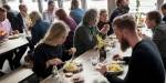 Folk som sit og et ved fleire langbord i ein restaurant med vindauge ut mot ei bygate.