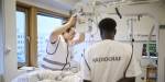 Radiografistudenter i hvite sykehusvester holder et røntgenapparat over sengen til en pasient.