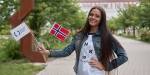 The photo shows a smiling girl outdoors on campus of the Czech university University of Hradec Králové, holding a flag with the university logo together with a Norwegian flag.