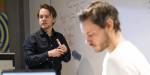 Mattijin ser mot datamaskinskjermen i forgruppen, e nærer snur seg fra tavlen med ligninger på.