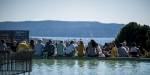 Students outdoors seen from behind, with a pool of water in the foreground and a view of the Oslofjord in the foreground. It is summer.