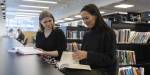 Two people searching for something in a book at a library.