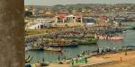Stort bilde av mange fiskebåter og mennesker i en havn i Ghana.