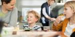 Two children and a woman smiling at each other at a table, placed in a family kitchen.