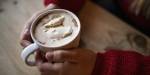 Hands holding a cup of hot cocoa with whipped cream