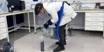 Her heller studenten flytende nitrogen fra en grå beholder over på en termos gjennom en trakt. Studenten har vernemaske og laboratoriefrakk.