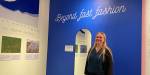 Forskar Kirsi Laitala foran tekstplakatar på museumsvegg og ein blå vegg med teksten Beyond fast fashion.