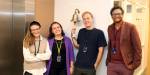 Portrett av Ranveig Strøm, Freyja Jørgensen, Magnus Svendsen og Tulpesh Patel fotografert ved heisen i Gründergarasjen. De smiler, og Magnus holder i tauet til en skipsklokke på veggen.