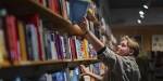 Woman picking out a book from a shelf in a book shop.