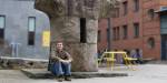 Tage sitter foran en skulptur ute på campus Pilestredet. Ved siden av står et gult bord.