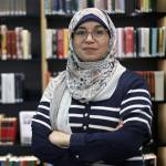 Nærbilde av Rawia Awadallah foran en str bokhylle med mange bøker.