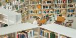 Oversiktsbilde av et bibliotek med mange hyller og bøker. I midten sitter en jente og leser på en dataskjerm.