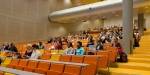 Studenter sitter i stort auditorium på gule og oransje seter.