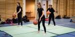 Tre studenter i treningstøy spretter basketballer på myke matter i en gymsal.