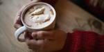 Hands holding a cup of hot chocolate with cream.