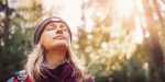 Woman stands in the forest and gets sunlight on her face