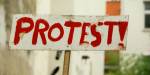 Et skilt med avskallet, hvit maling hvor det står ordet protest med utropstegn i stor, rød skrift.
