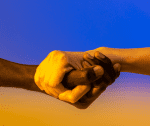 two hands clasping each other in the foreground with the colors of the ukrainian flag in the background