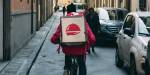 Et sykkelbud fra Foodora sykler i en smal gate.