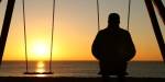 En mann sitter på en huske med ryggen mot kameraet og ser på solnedgangen.