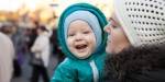 Smilende barn i mors armer, kledd i vinterklær. Foto: Colourbox.com