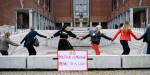 En rekke med mennesker som holder hverandre i hendene foran Oslo rådhus. Foran dem står det en plakat.