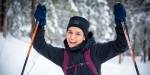 Woman dressed in winter clothes and holding ski poles is lifting her arms above her head.