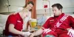 A male paramedic student in a hospital bed while a female student practise on his arm.