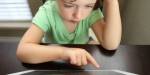 En liten jente sitter ved et bord og bruker en iPad