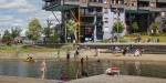 A small stretch of sand, wooden stairs and people enjoying the fjord in front of an urban apartment building.