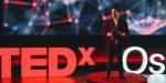 Andreas Graf på scenen som er farget i rødt, sort og hvitt lys. Vi ser TEDx logoen i rødt foran i bildet.