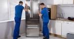 To menn som skyver et stort kjøleskap inn i et hjørne på et kjøkken