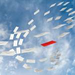 Hvite brev som flyr gjennom luften, ett rødt brev