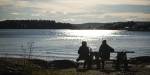 Silhouette of two people on a bench looking at fjord on a sunny day.