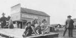 Black an white photo of children sitting on a wooden platform outside a store.
