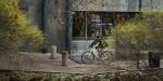 Marco biking through OsloMet campus in fall. He is dressed in a light down jacked and there are green and yellow leaves on the ground.