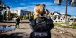 Ein kvinneleg journalist står med ryggen til kamera og fotograferer eti bomba område i Kherson, Ukraina. I bakgrunnen er det soldatar.