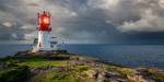 Lindesnes Fyr med havet i bakgrunnen. fyrlykten lyser men det er dramatiske skyer over havet.