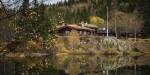 A wooden cabin with grass roof in the forest reflecting in a small lake.