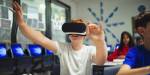 Boy sitting in a classroom with VR glasses on. He is holding his arms in front of himself.