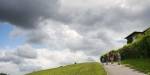A huge, cloudy sky and a piece of the lawn in a parc. People walking uphill on a small path in the parc.