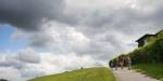 A huge, cloudy sky and a piece of the lawn in a parc. People walking uphill on a small path in the parc.