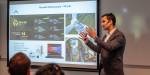 Arvind Keprate gestures with his arms as he explains intensely to the audience. On the left we see a presentation of the lab.