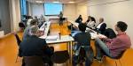 Forskarar sit ved bordet medan Siw held foredrag ved skjermen inst i rommet.